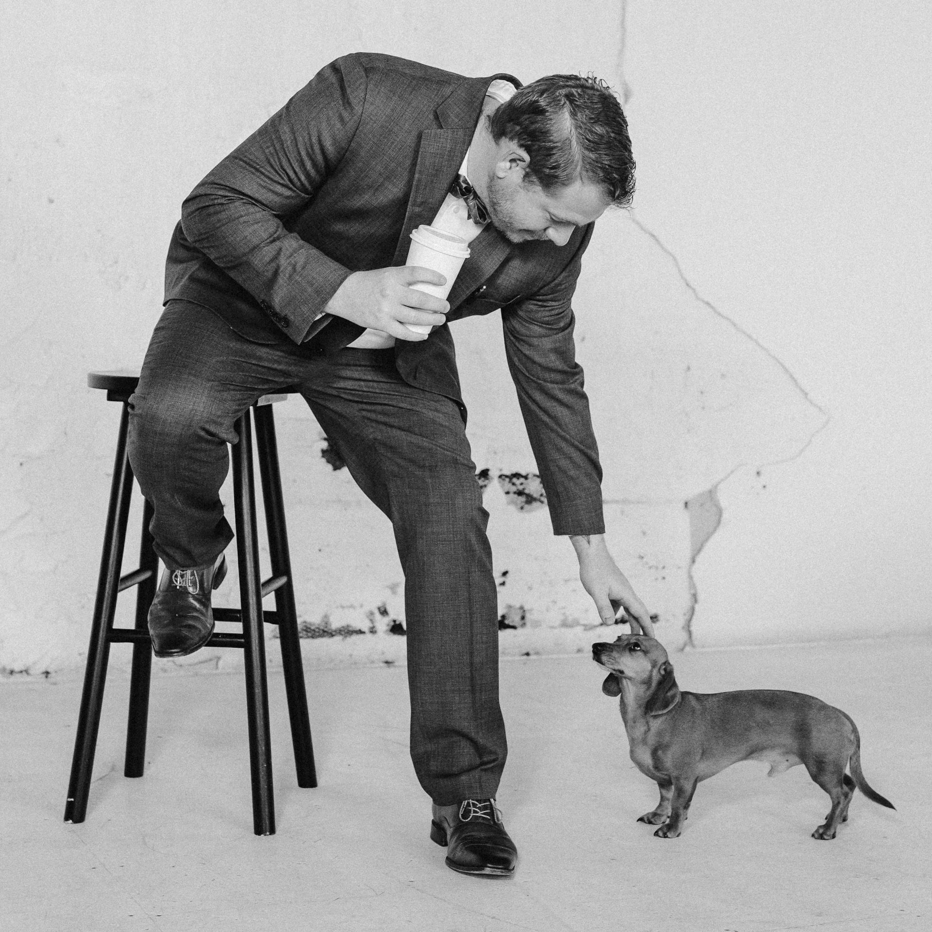 A man sitting on a stool petting a small dog