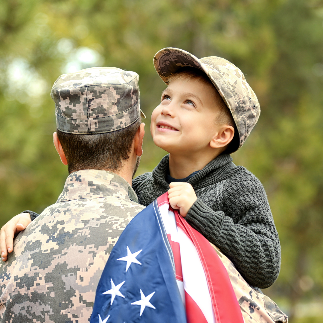 A man in a military uniform is holding a little boy who is holding an american flag.