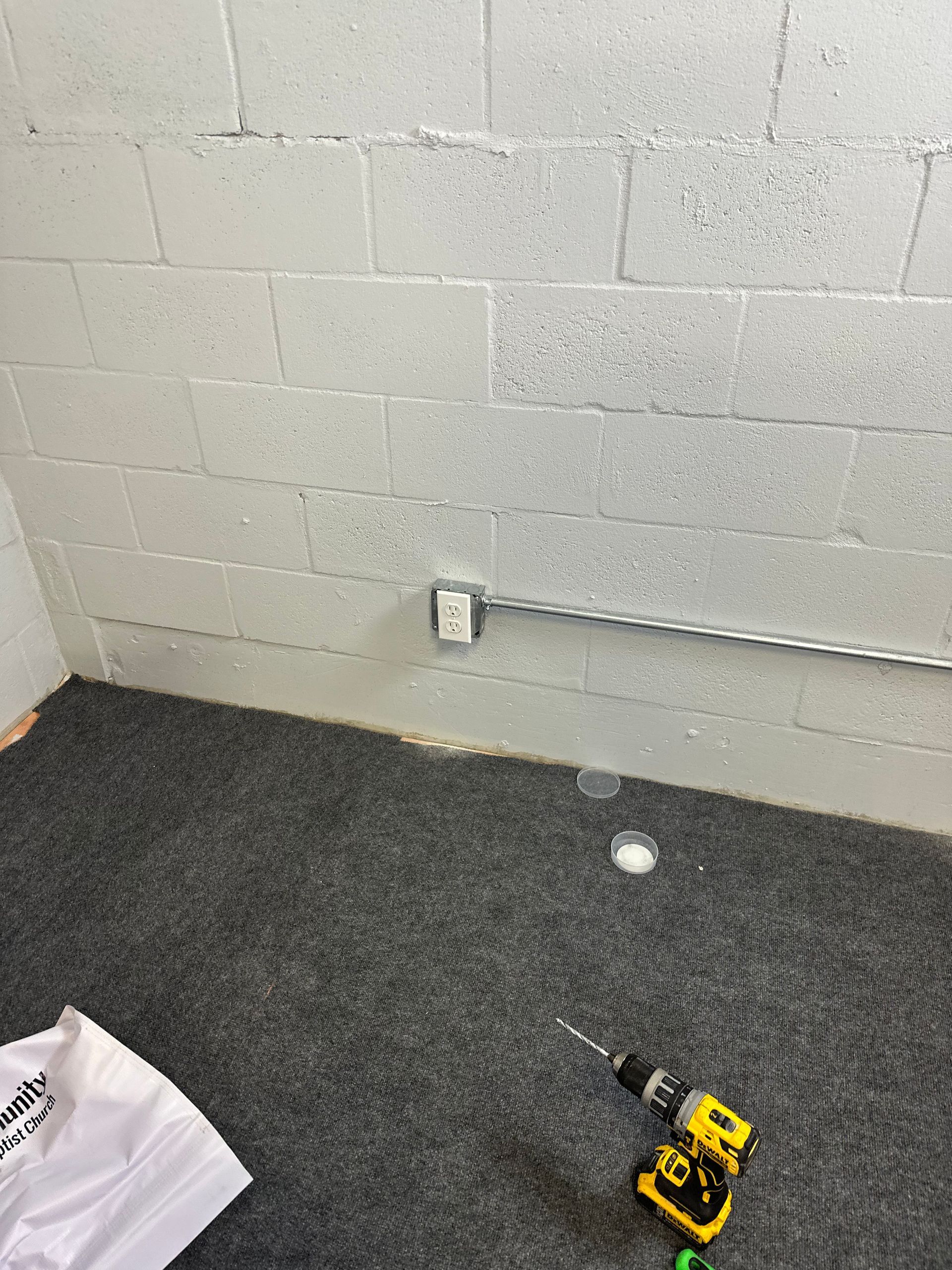 A drill is sitting on the floor next to a brick wall.