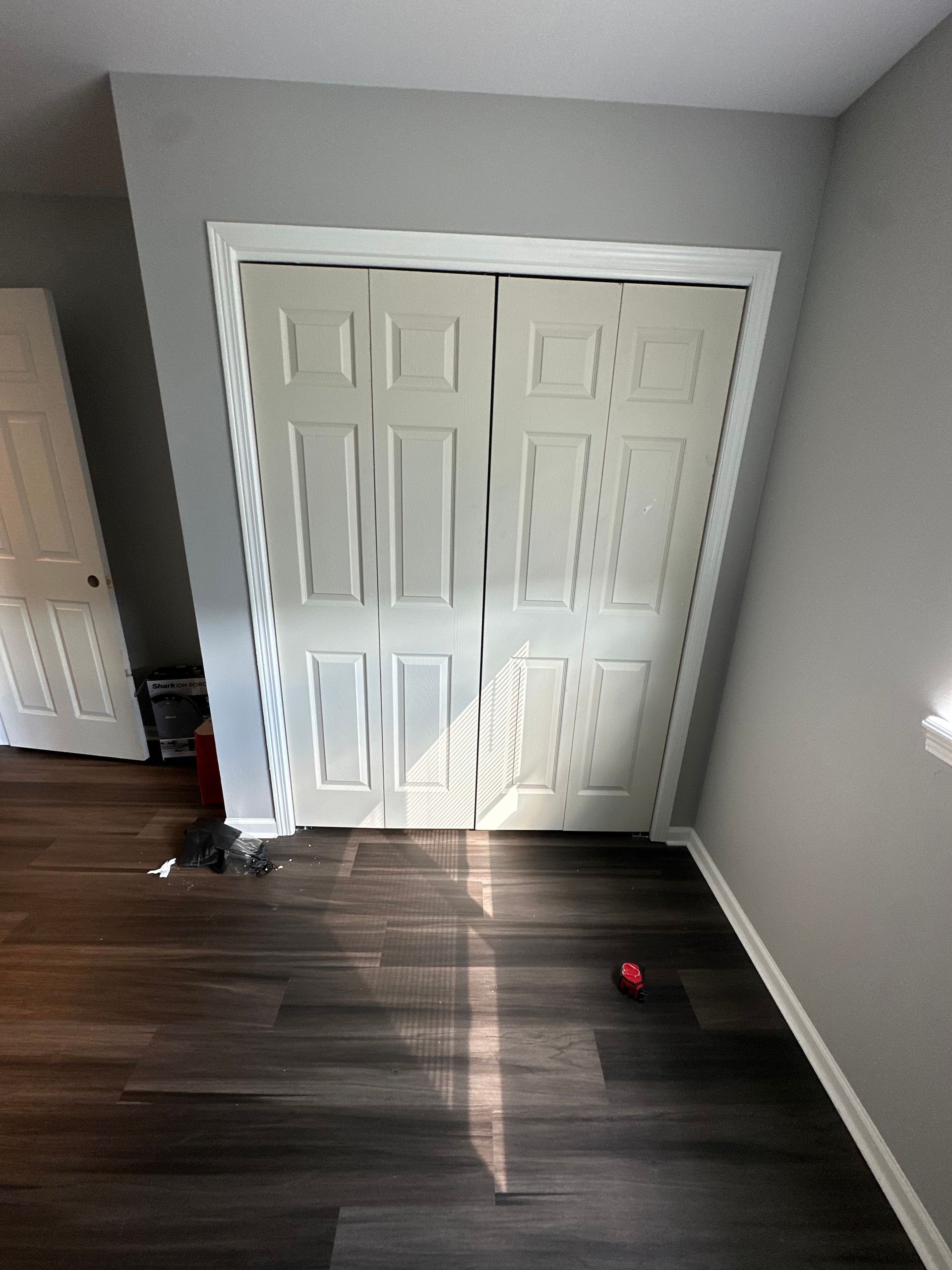 Wooden closet doors with white trim and gray walls; dark wood flooring with a small red ball.