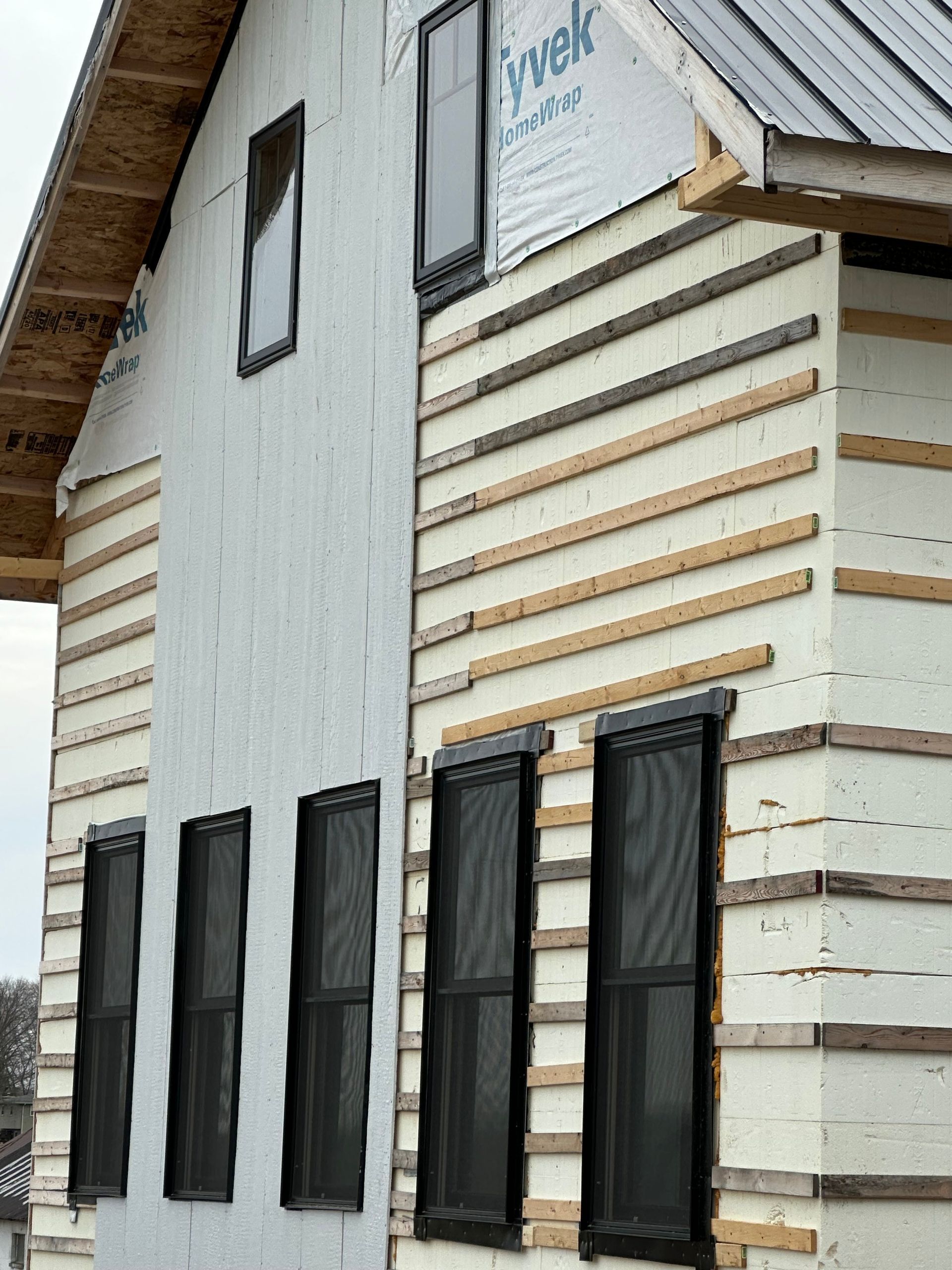 Exterior of a house under construction.  White sheathing and Tyvek are installed with window frames visible.