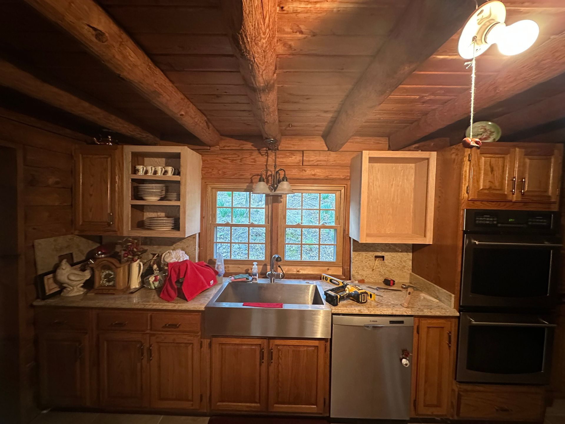 A kitchen with wood cabinets, a stainless steel sink, and a double oven. Sunlight streams through the window.