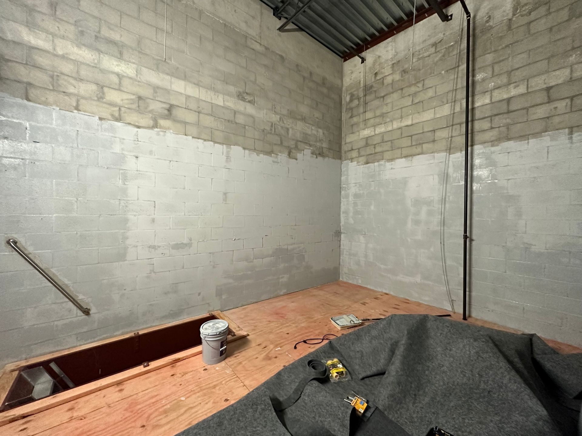 Interior of a room under construction with cinder block walls, a wood floor, and exposed pipes. 