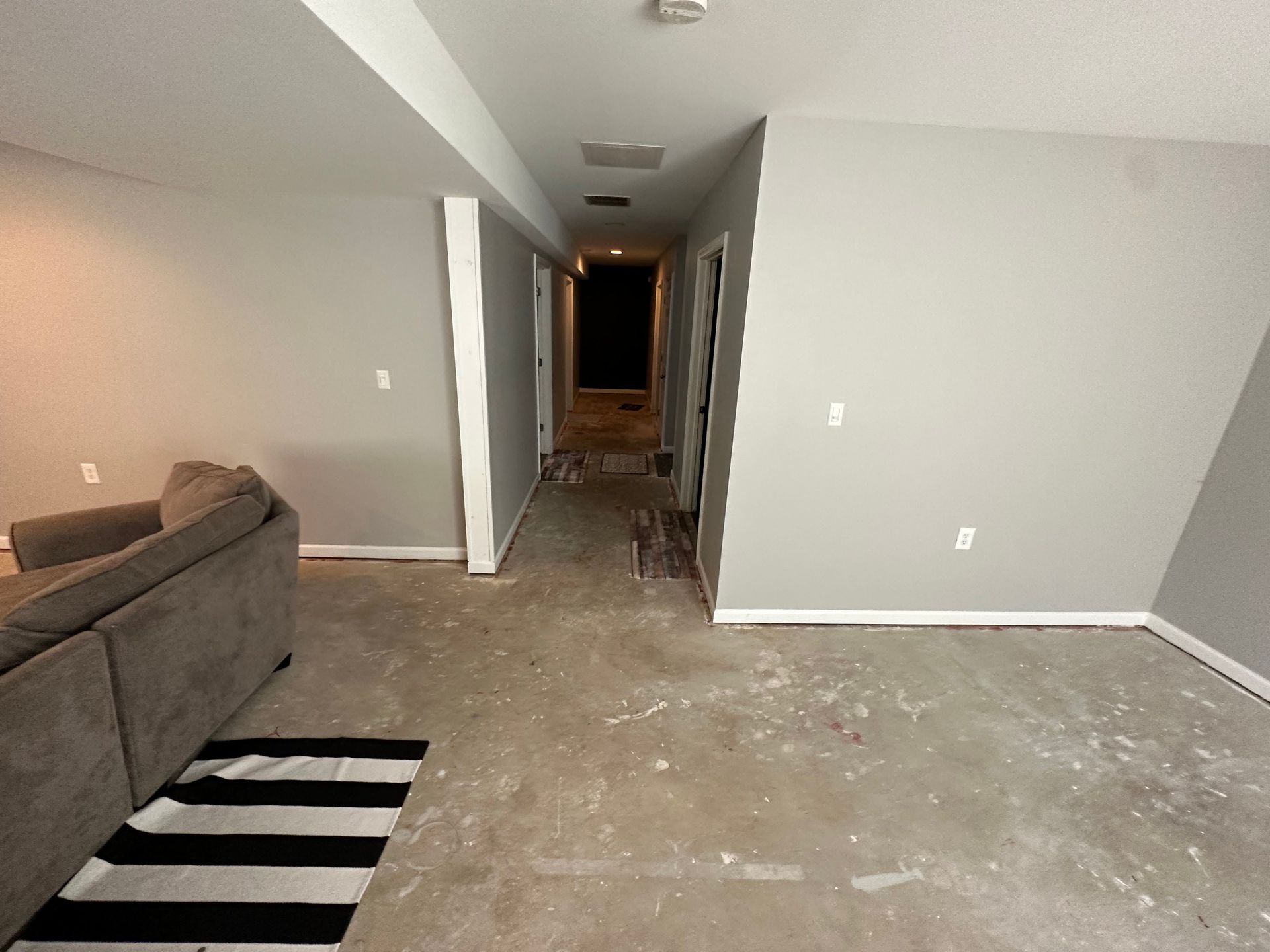 Interior view of a room with gray walls, a hallway, and a sofa. The floor has visible damage.