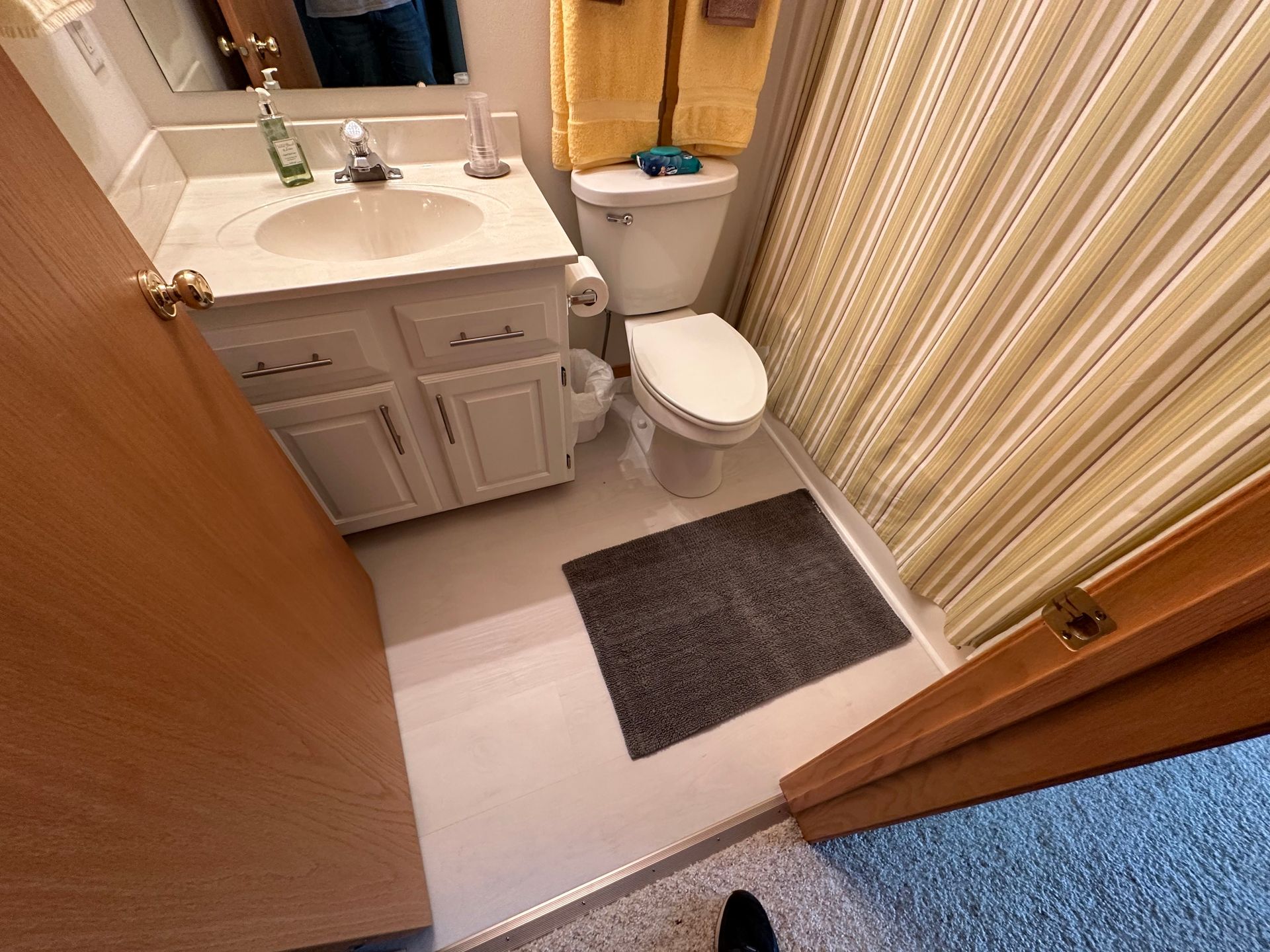 Small bathroom with a white sink and toilet, yellow shower curtain, and a gray rug on a white floor. 