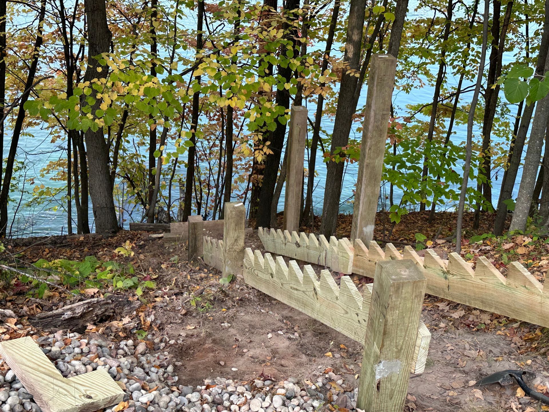 Wooden stair construction near a body of water. The stairs are partially built with posts and zig-zag supports.