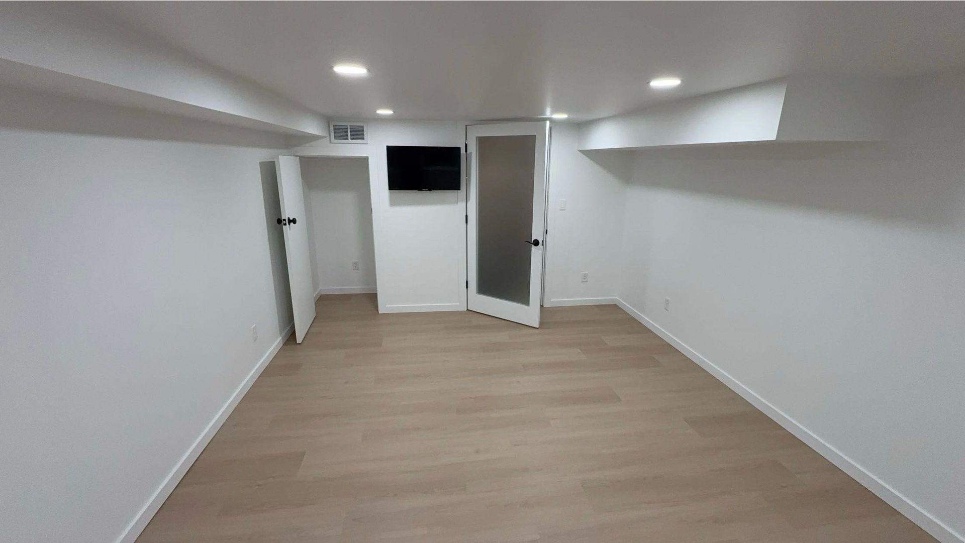 A room with white walls and wooden floors and a flat screen tv on the wall.