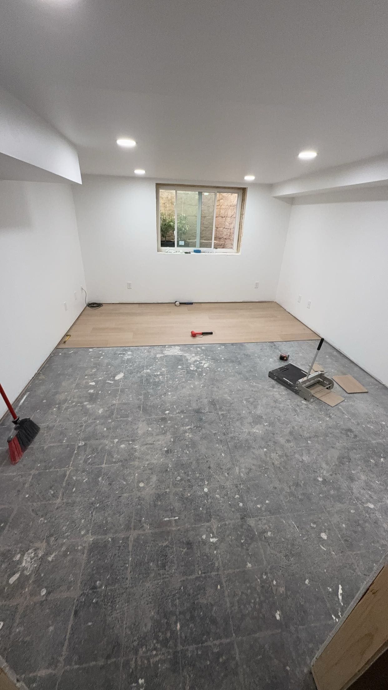 An empty room with a window and a broom on the floor.