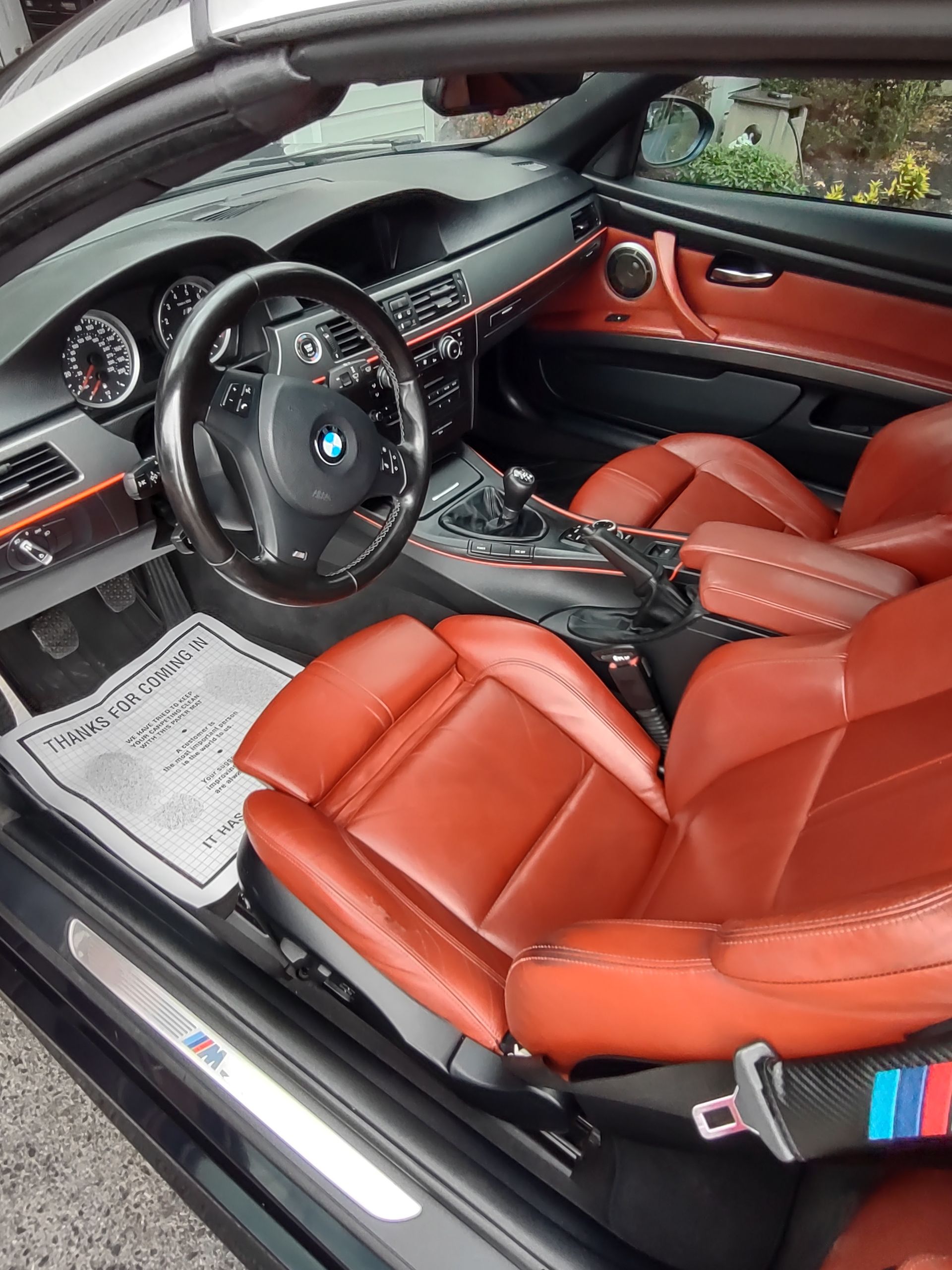 Interior of a black BMW M3 with red leather seats, steering wheel, and orange accents.