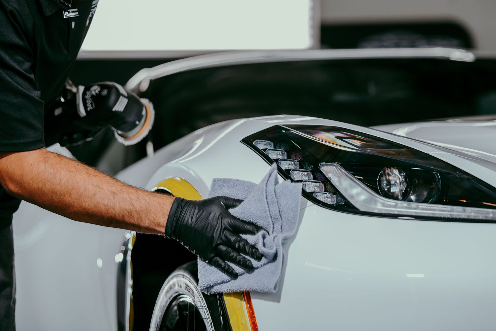 A man is polishing a car with a sander and a cloth.