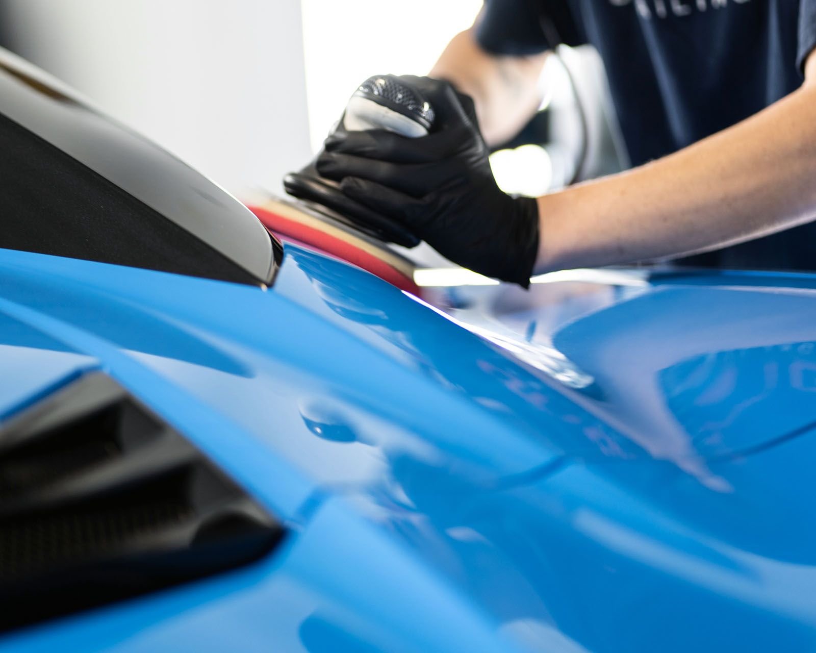 A man wearing black gloves is polishing a blue car