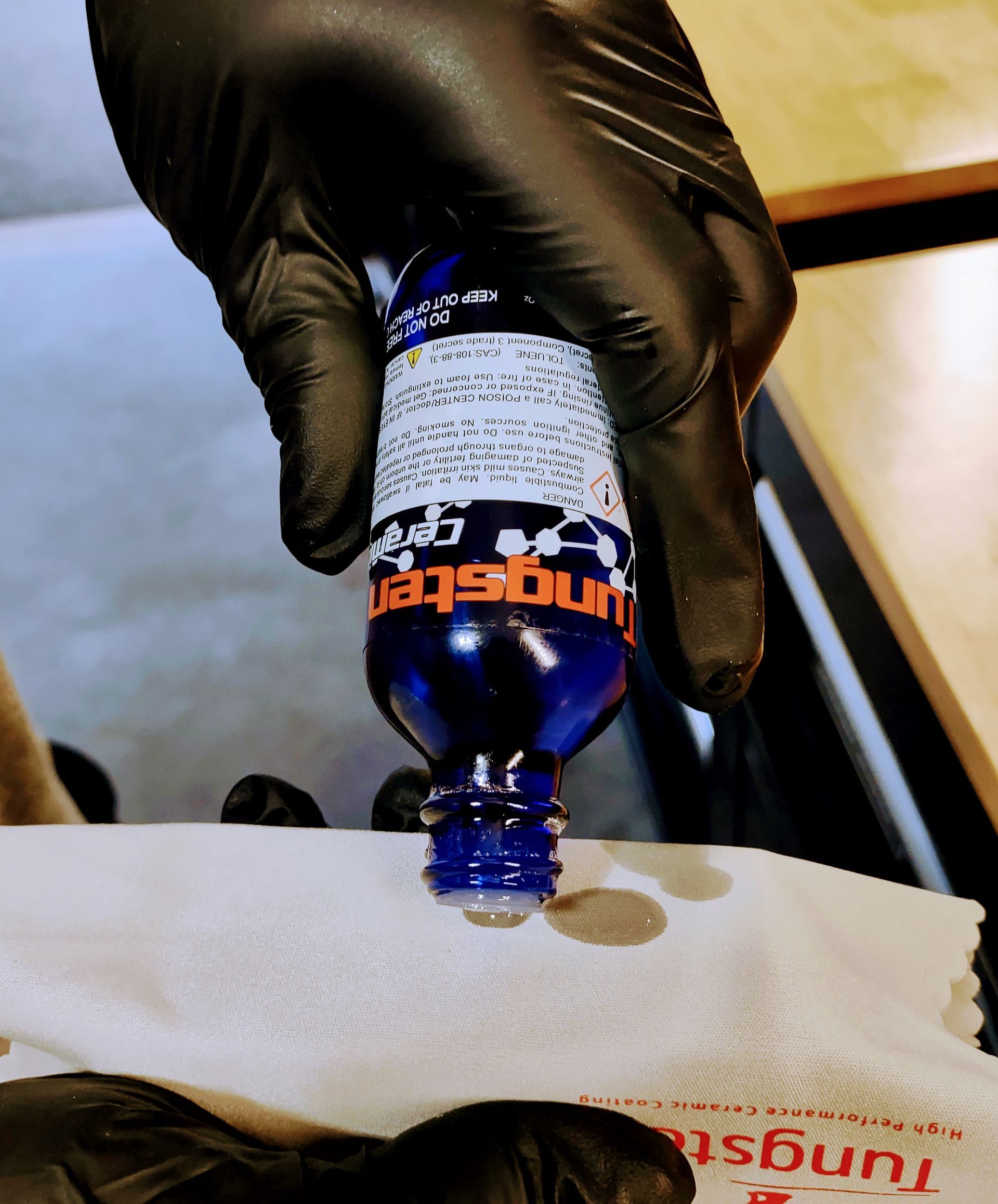 A person wearing black gloves is holding a bottle of tungsten gel