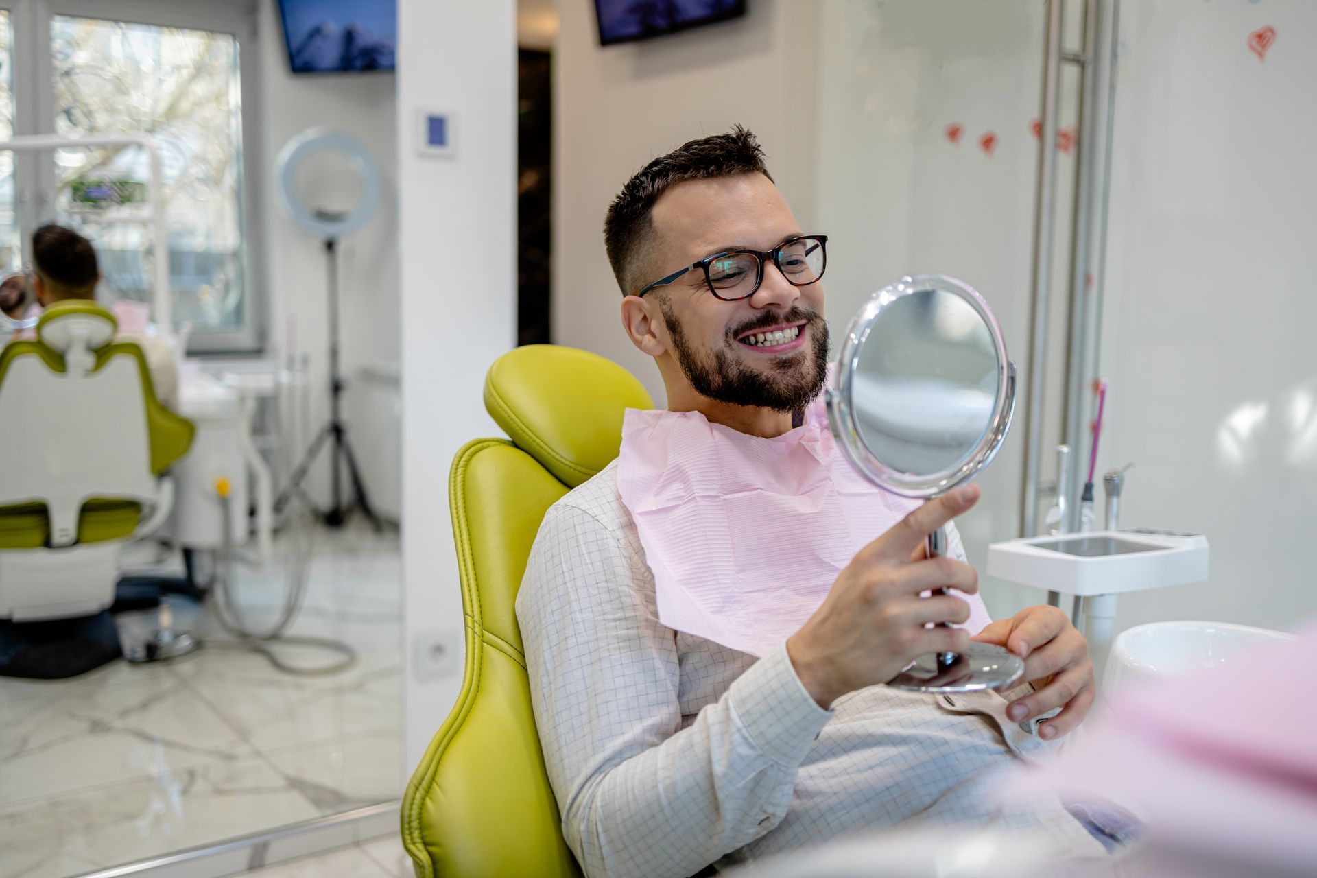 Un uomo è seduto sulla poltrona del dentista e si guarda i denti allo specchio.