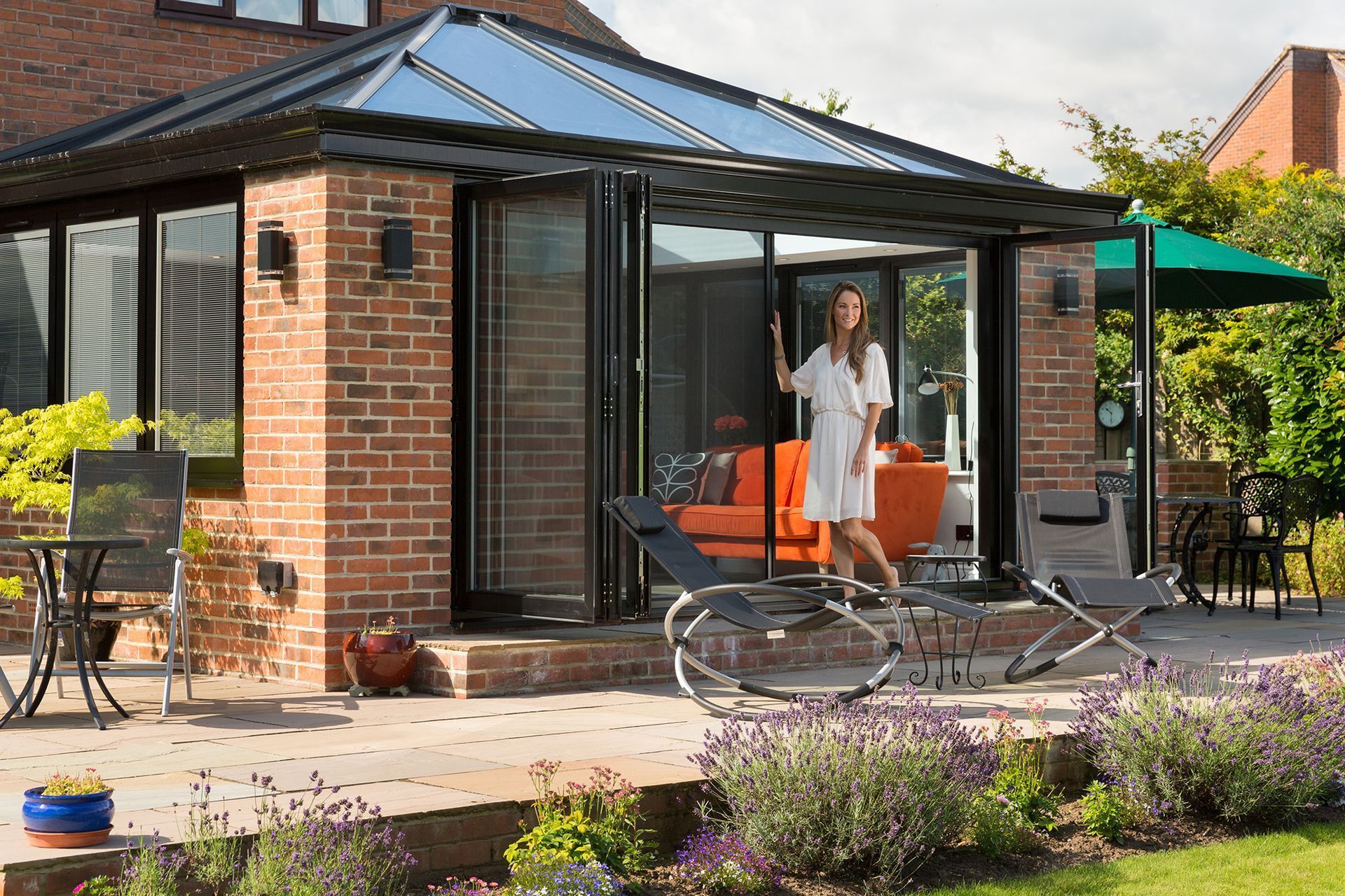 A Woman Is Standing On A Patio In Front Of A Brick House — Roo’s Door & Window Maintenance In Sippy Downs, QLD
