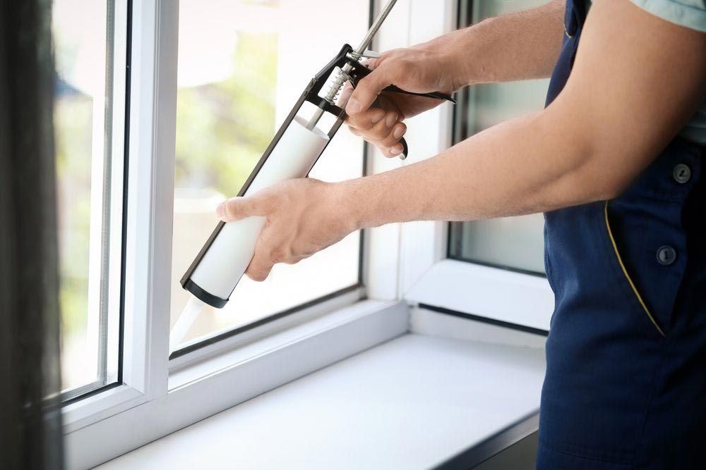 A technician applying weather sealant to a window.