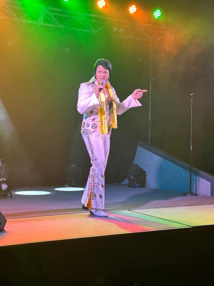 A man in a white suit is singing into a microphone on a stage.