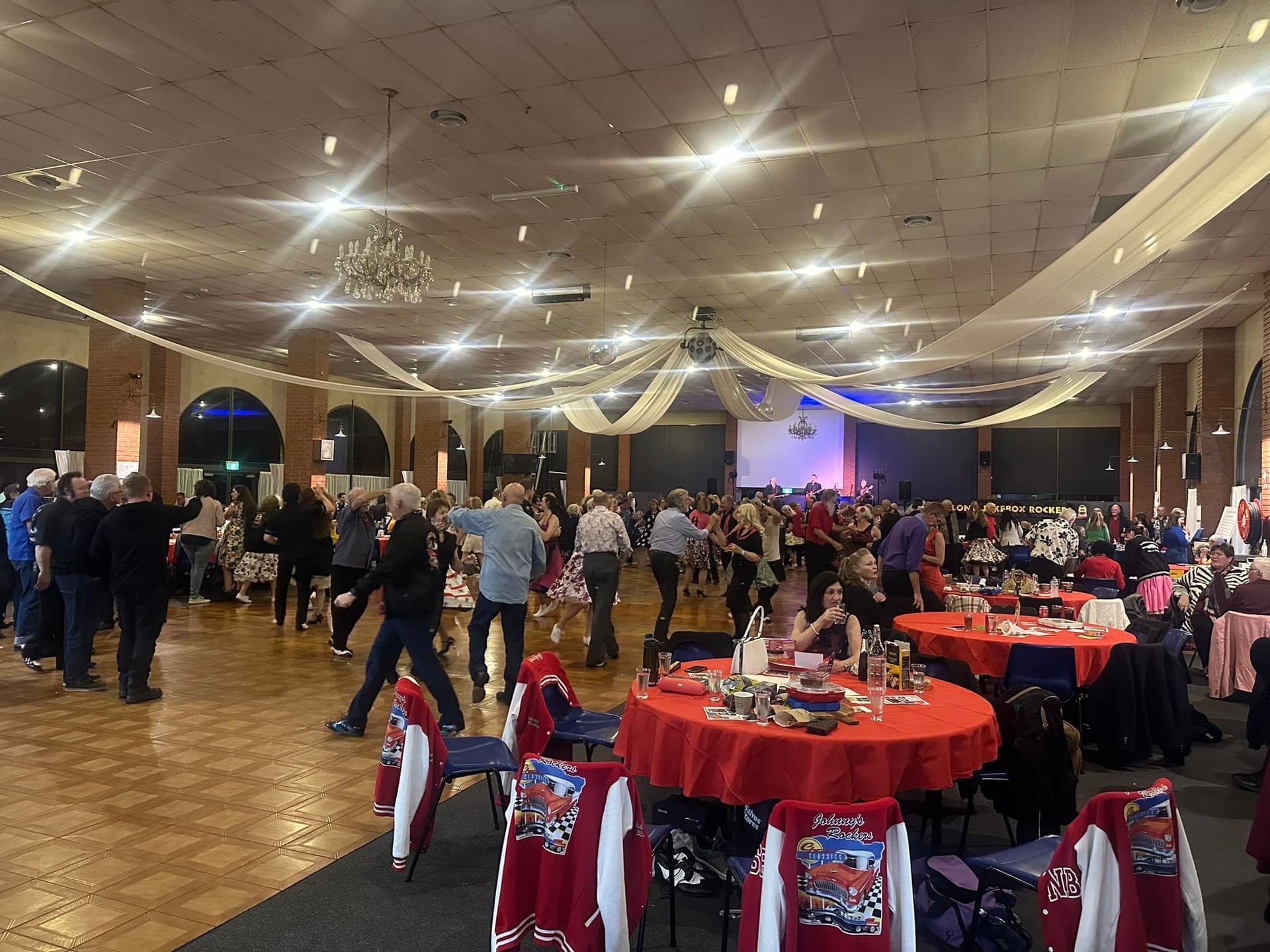 A large room filled with people sitting at tables and dancing.