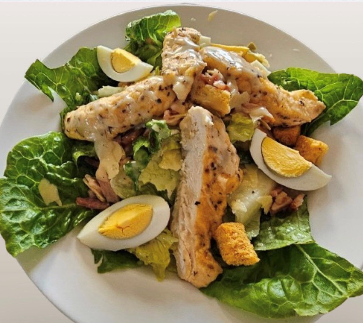A salad with chicken eggs and lettuce on a white plate