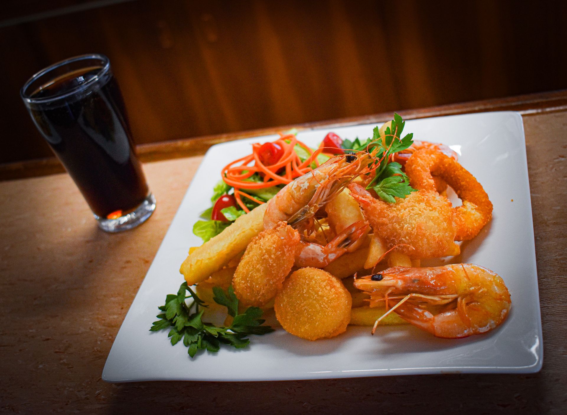 A plate of food with shrimp, French fries and a glass of soda on a table.