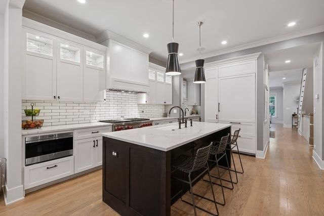 Modern white kitchen with dark island and light wood flooring.