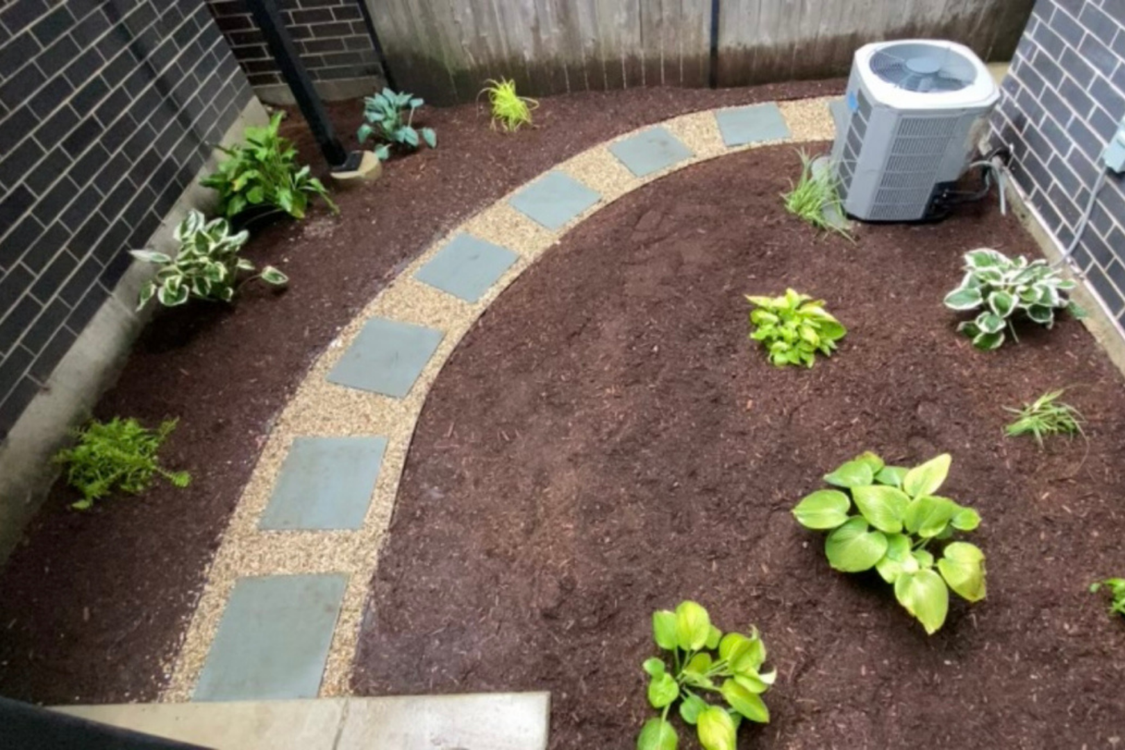 Landscaped backyard with stone pathway, mulch, and various green plants.