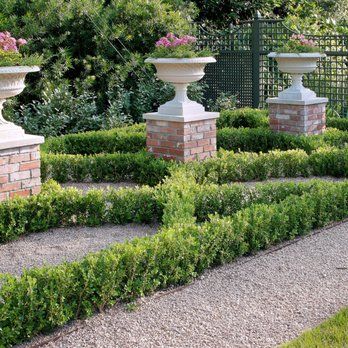 Formal garden with gravel pathways and manicured hedges, brick pedestals holding floral urns.