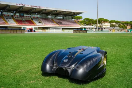 Robotic lawnmower on a green soccer field, stadium in the background.