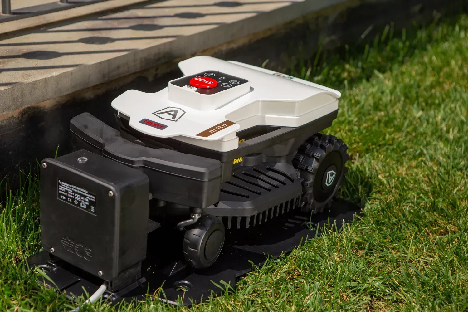 Robot lawn mower parked on green grass near a building's foundation.