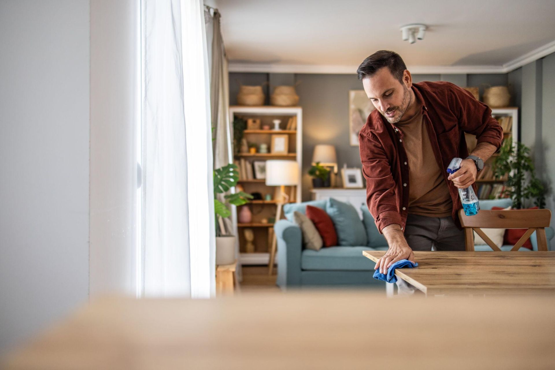 Woman wearing yellow gloves cleaning floor in a living room, smiling. Cleaning supplies in a blue bin.