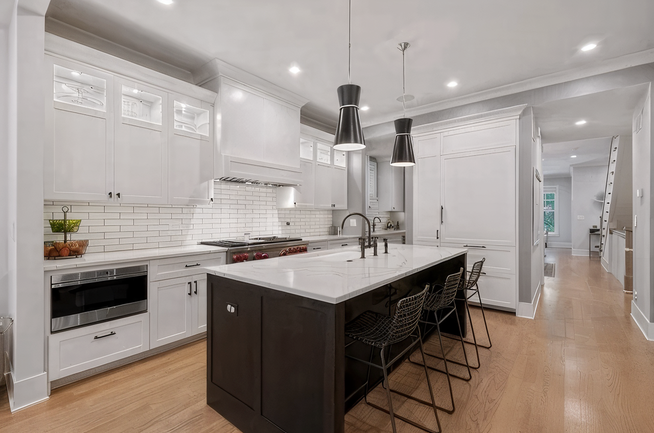 Modern white kitchen with dark island and light wood flooring.