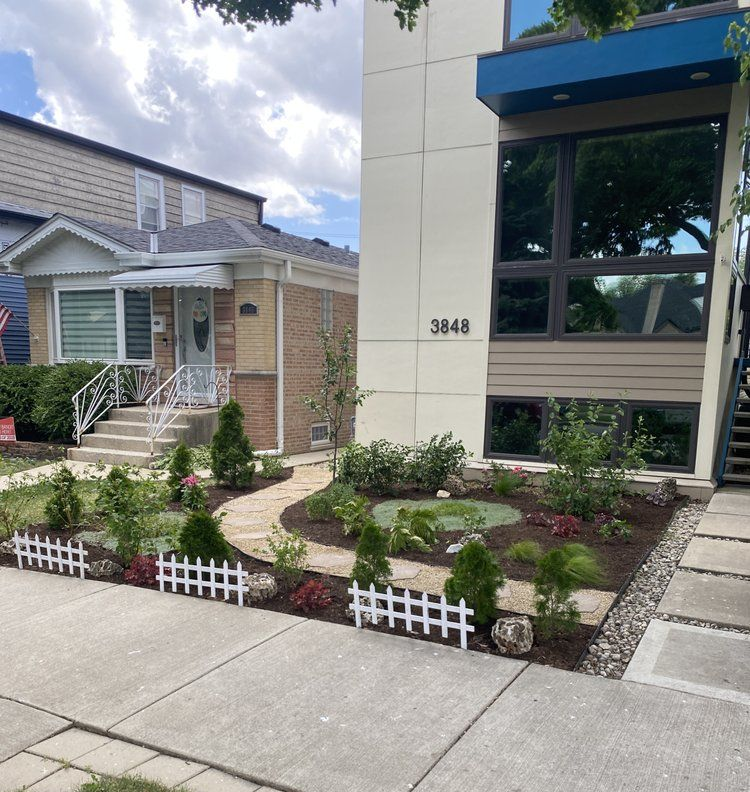 Landscaped yard with stone path, white picket fence, and modern house with blue trim.