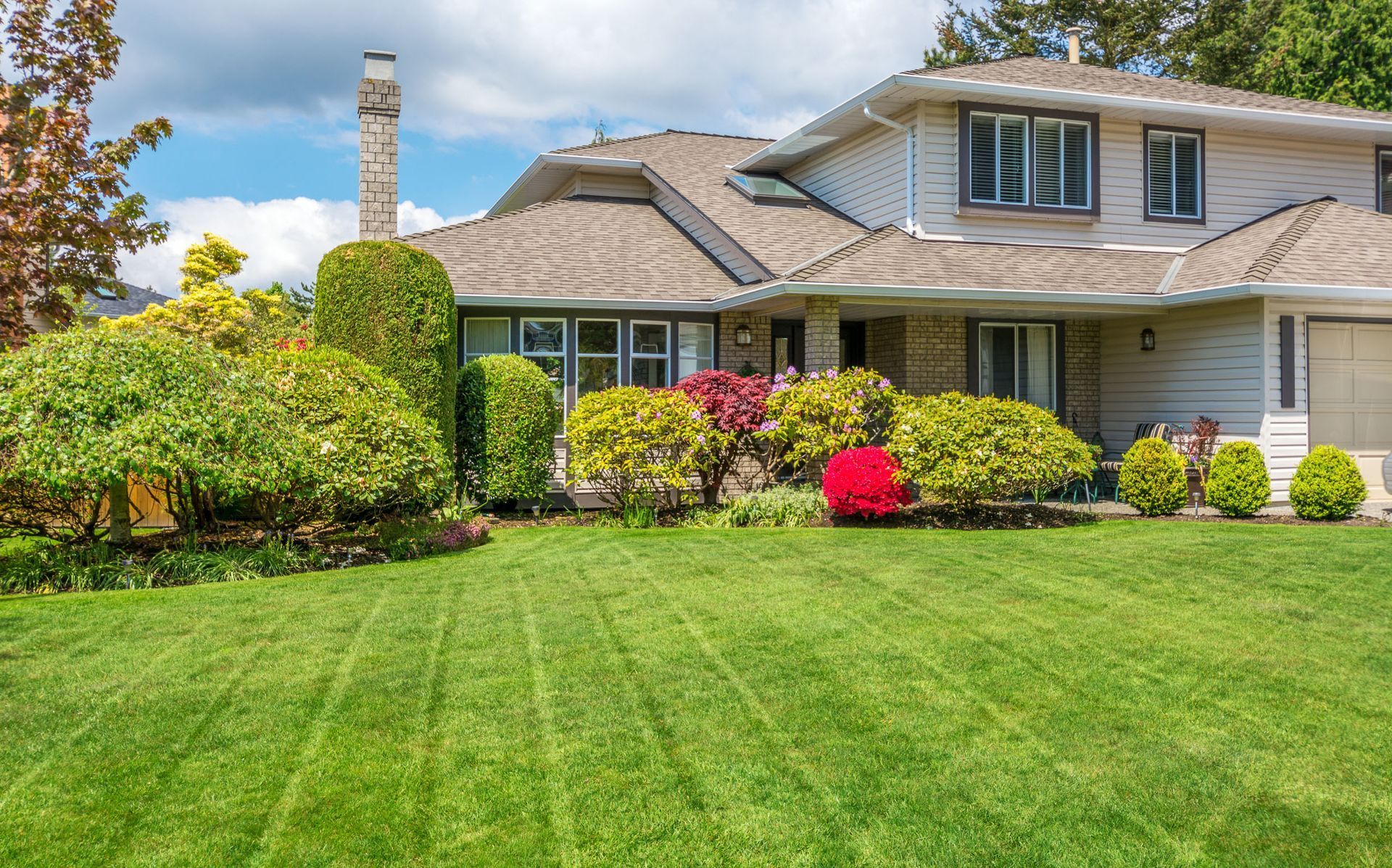 A two-story house with green lawn and bushes. Cloudy sky.