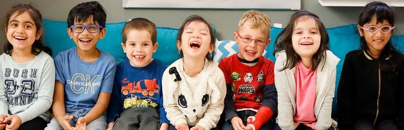 A group of children are sitting on a blue couch and smiling.