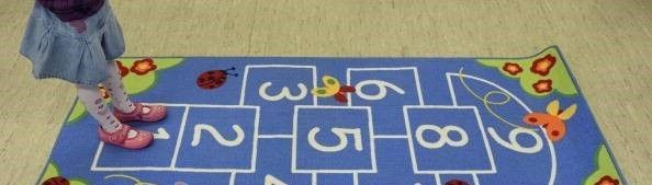 A little girl is playing hopscotch on a blue rug