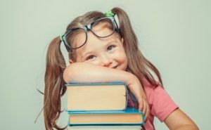 A little girl wearing glasses is leaning on a stack of books.