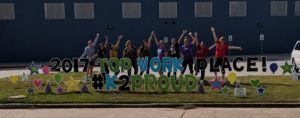 A group of people are standing in front of a sign that says `` 2017 top work place ! ''