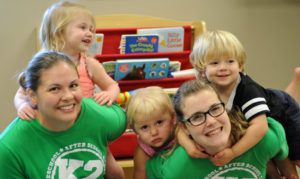 A group of children are posing for a picture with a woman in a green shirt.