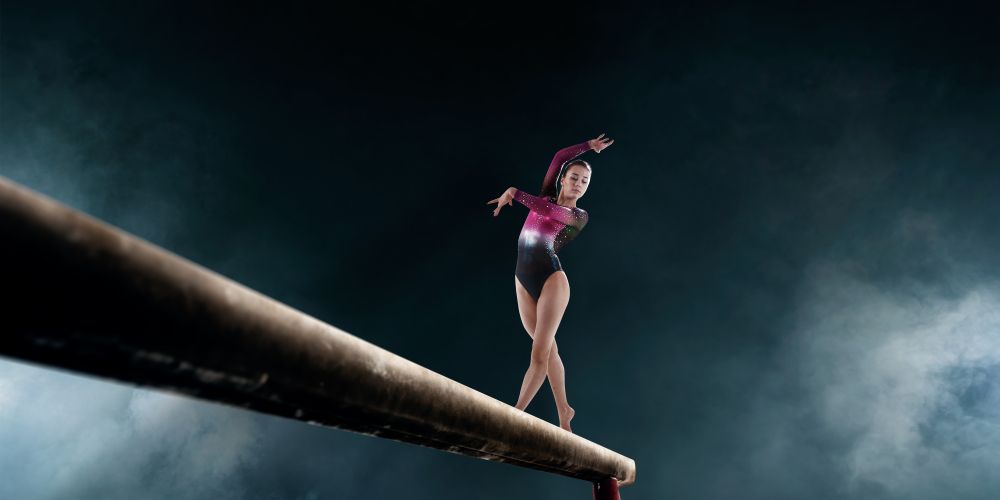 A female gymnast is standing on a balance beam.