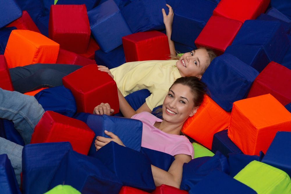 A woman and a child are laying in a pile of foam cubes.