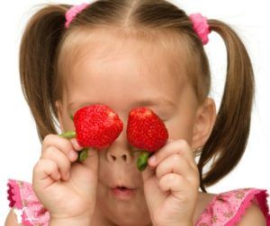 A little girl is holding two strawberries in front of her eyes.