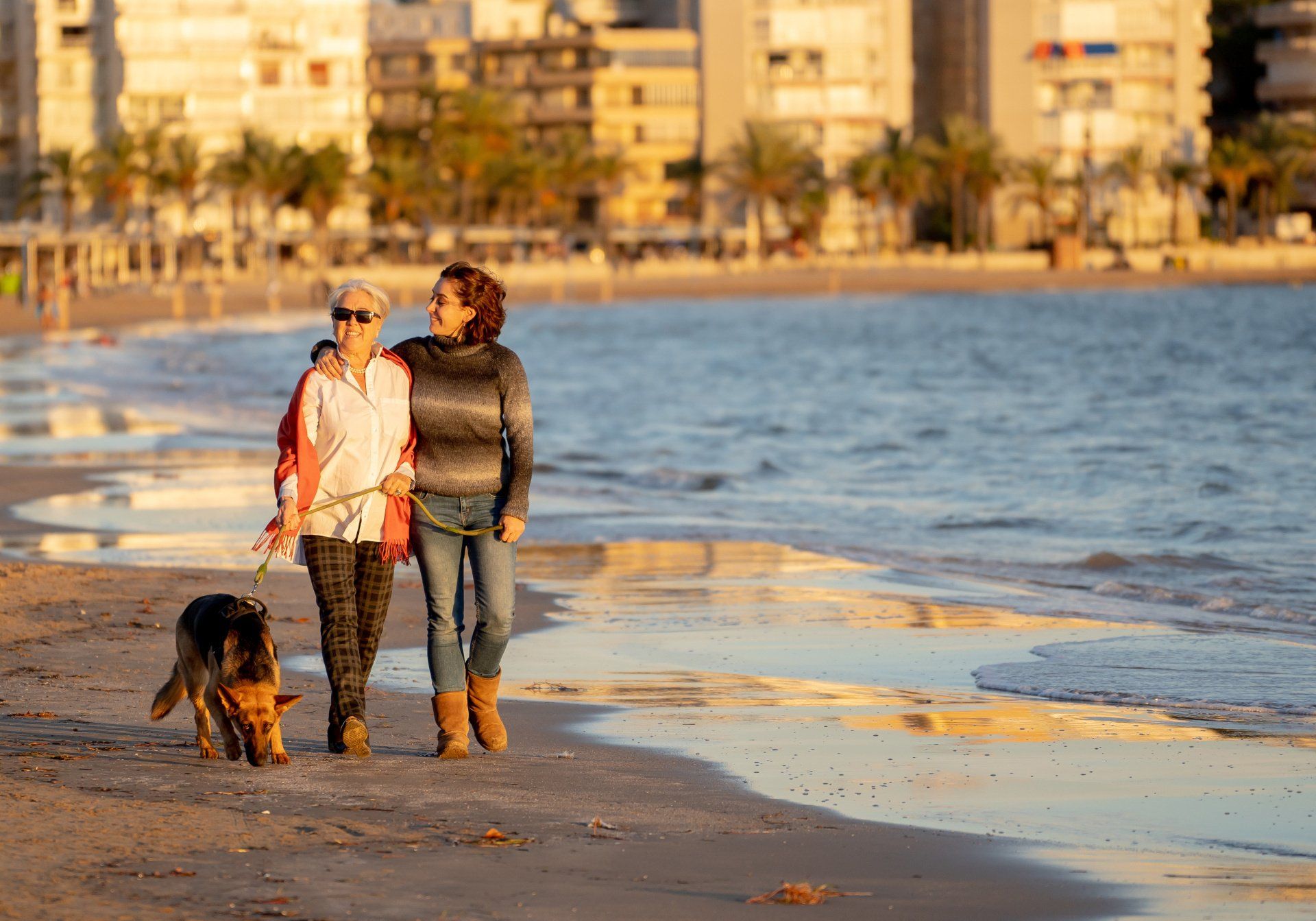 Two women are walking a dog on the beach.