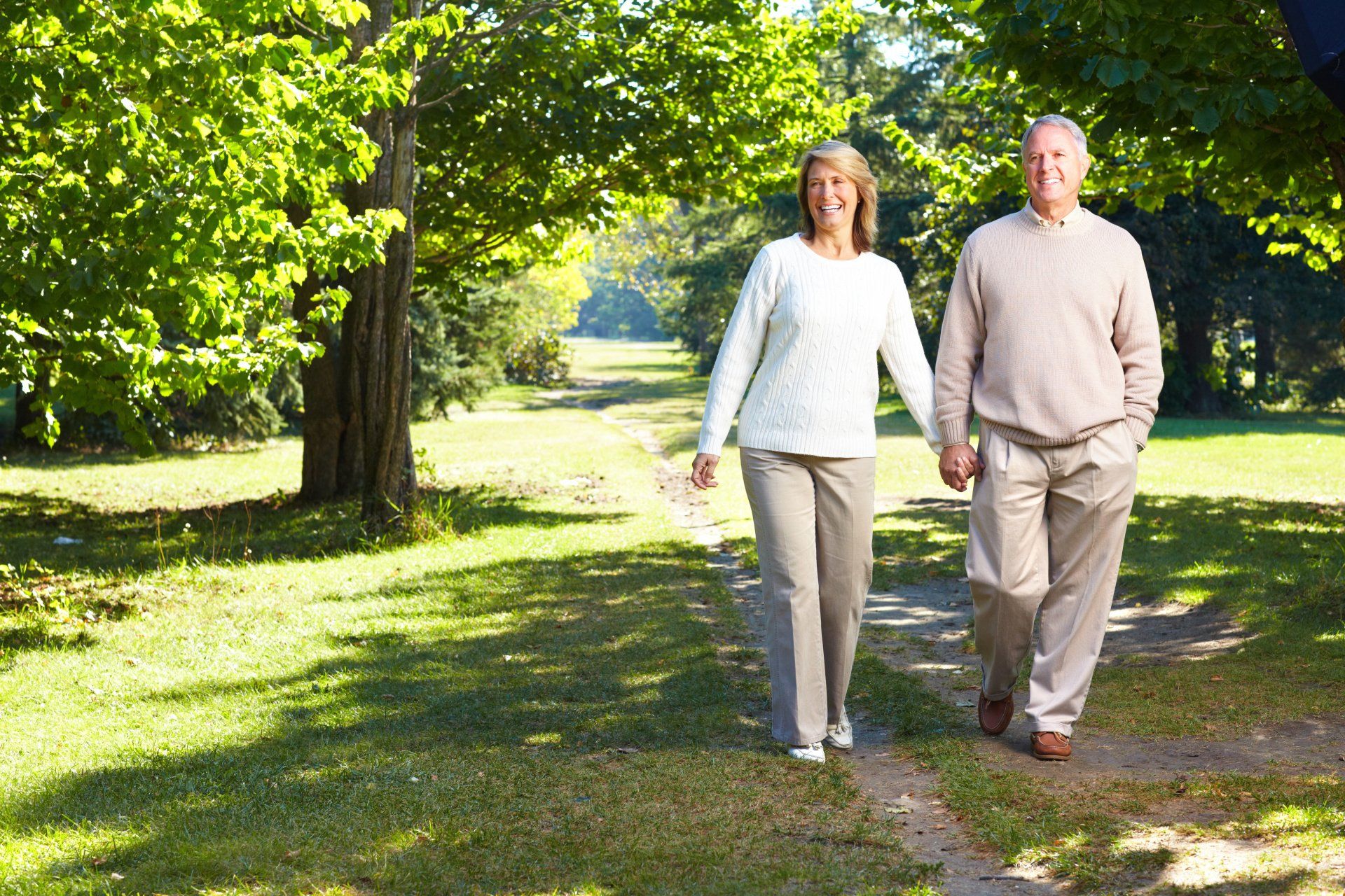 A man and woman are walking down a path in a park holding hands.