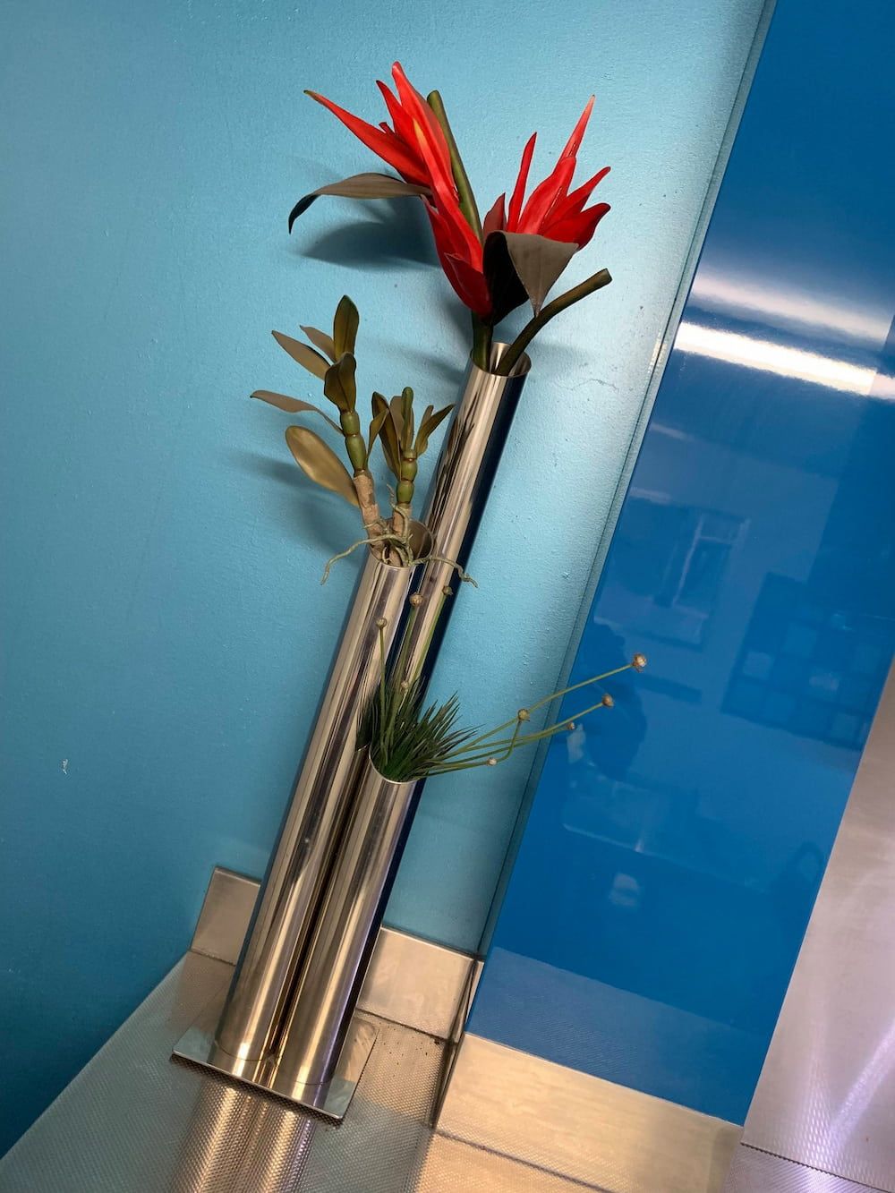 A Silver Vase With Red Flowers in It Against a Blue Wall — Metaltrendz in Buderim, QLD