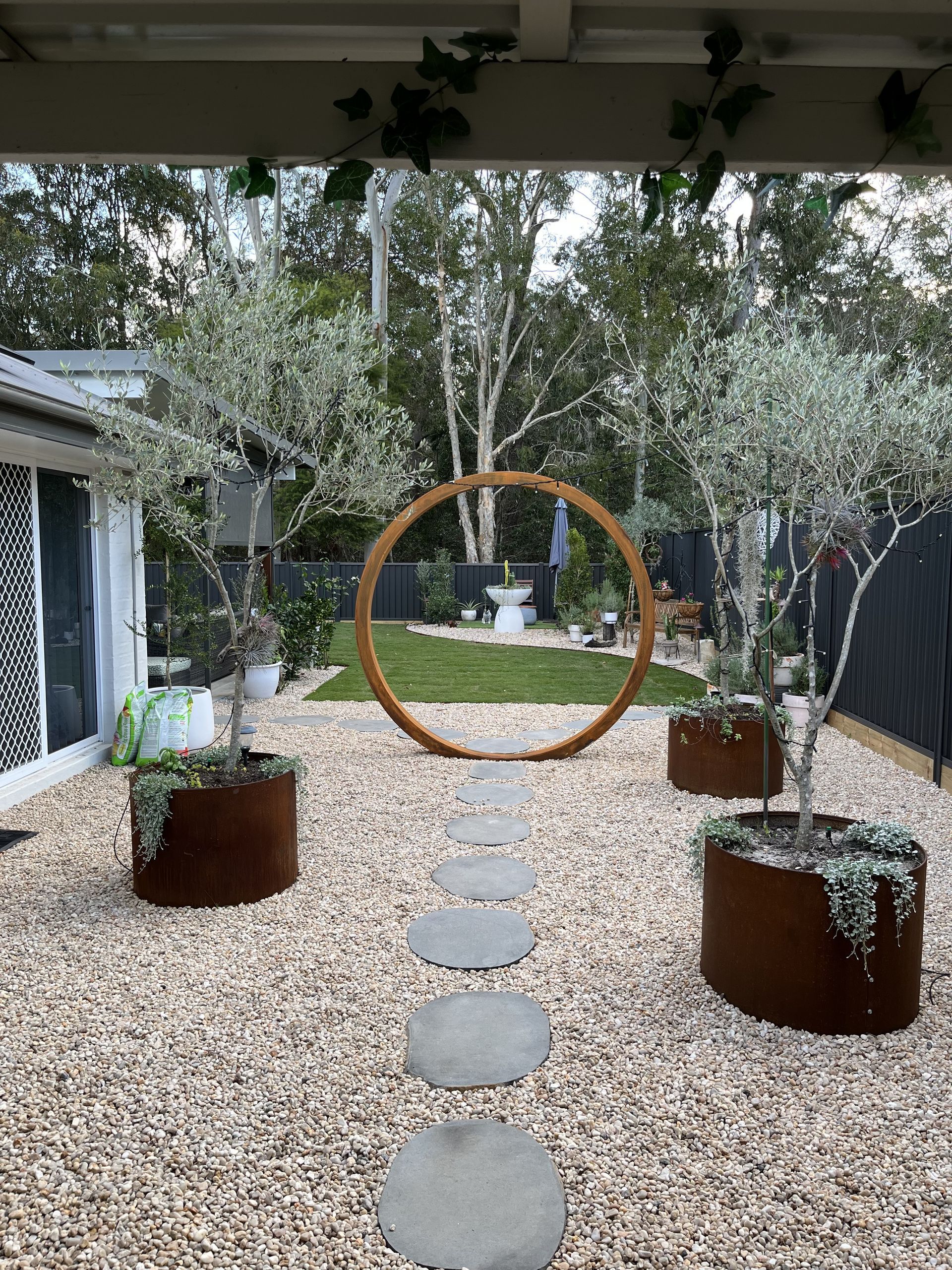 A backyard with a gravel path, stepping stones, and trees in metal planters — Metaltrendz in Kunda Park, QLD