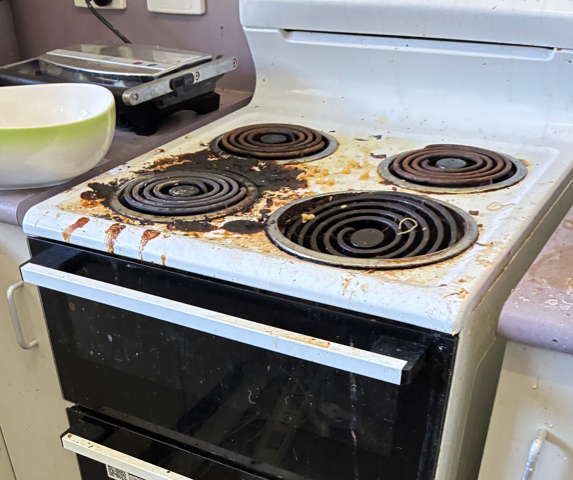 A Dirty, White Electric Stove Top With Four Burners Covered in Food Stains — Schmucker Cleaning in Gulliver, QLD
