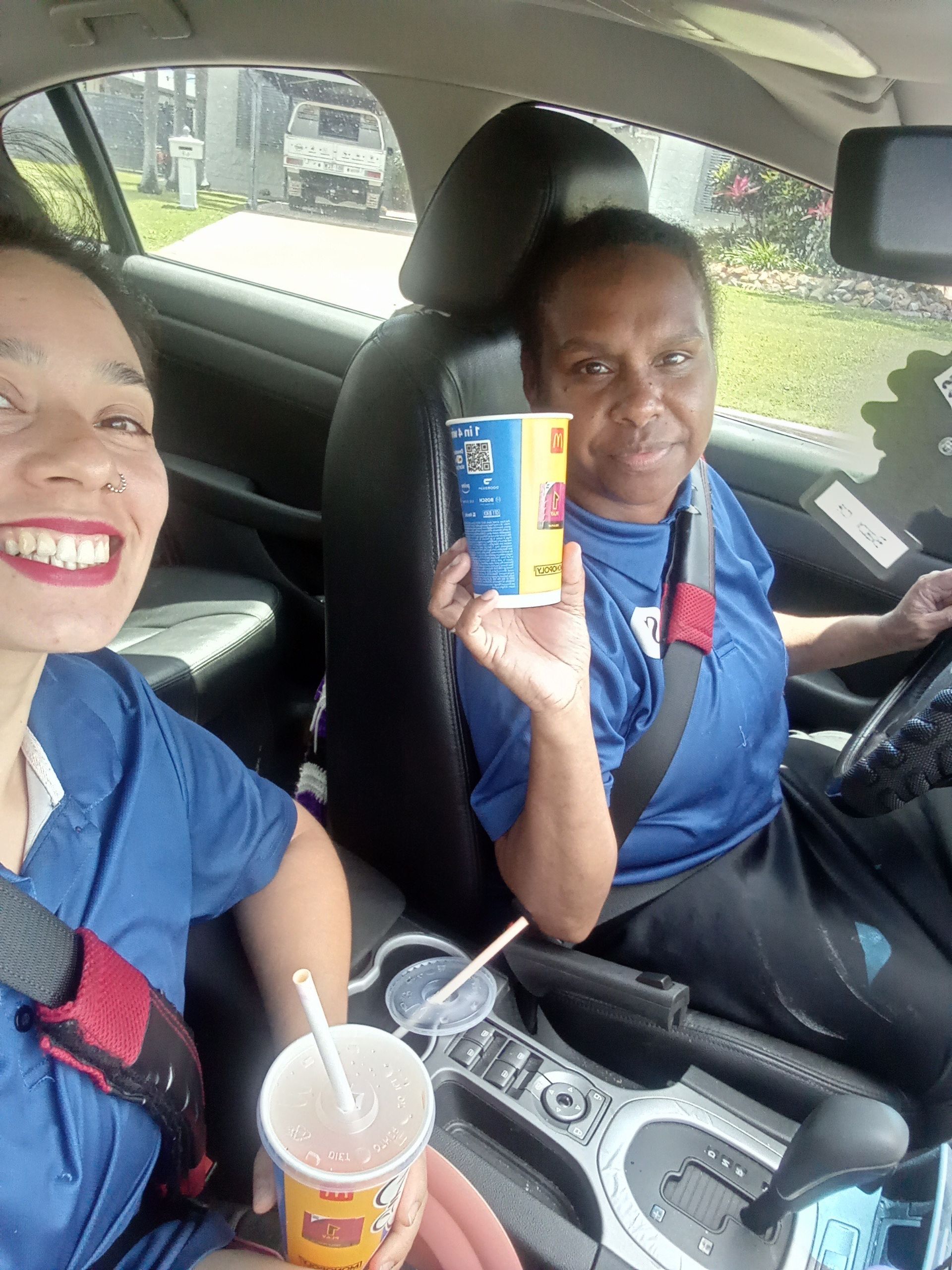 Two People In Uniforms In A Car Holding A Cup Up And Smiling — Schmucker Cleaning in Gulliver, QLD
