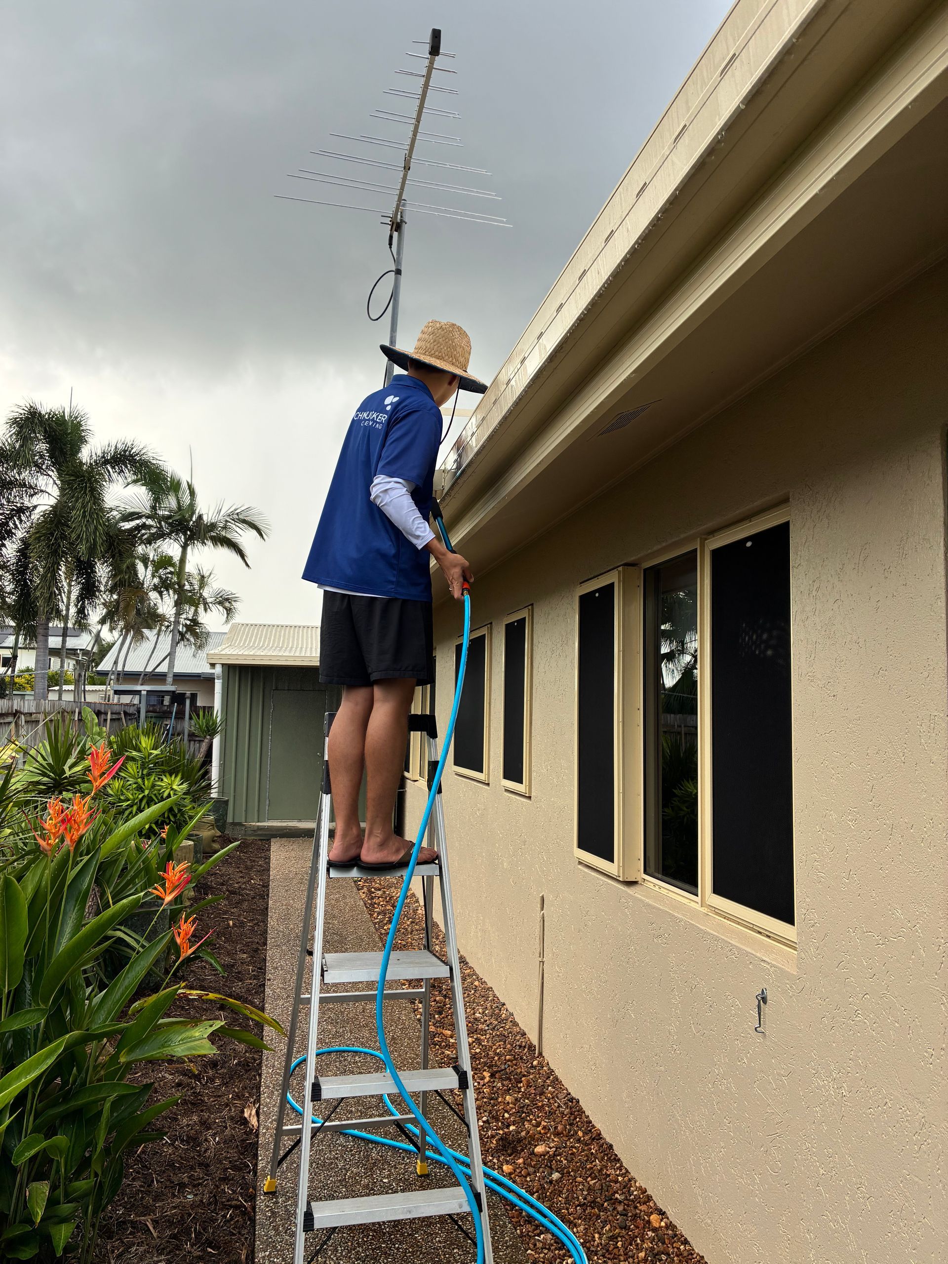 A Person Wearing a Sun Hat Stands on A Ladder — Schmucker Cleaning In Gulliver, QLD