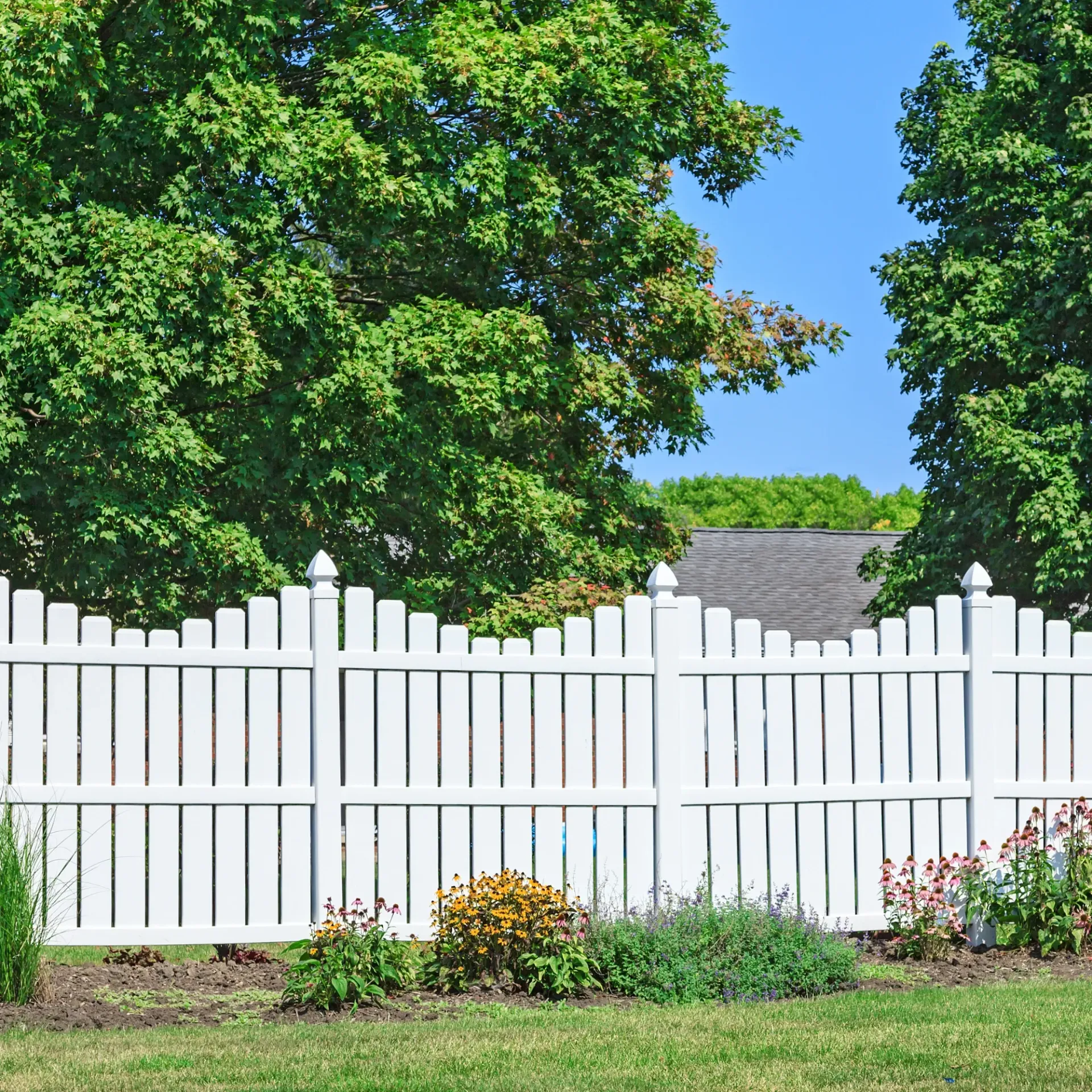 Boots & Boards Fencing - A white picket fence surrounds a lush green yard.