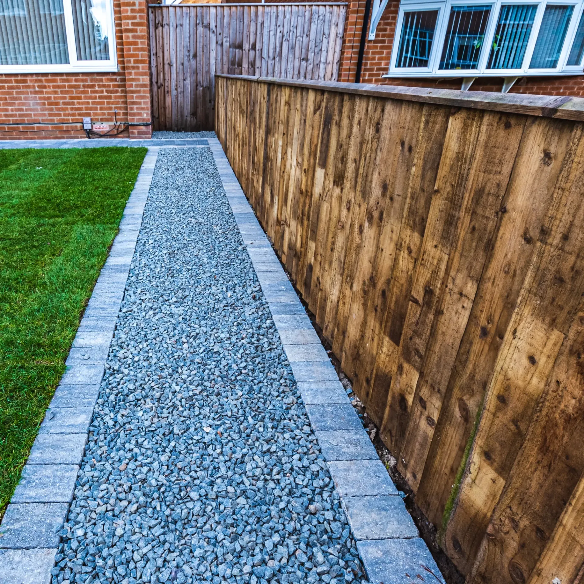 Boots & Boards Fencing - A stone walkway leading to a wooden fence next to a brick house.