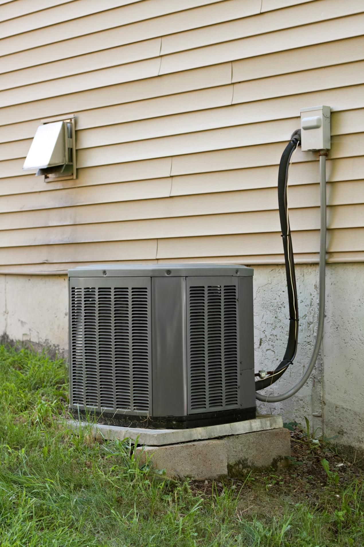 Air conditioning unit outside a house, with electrical connections and vent.